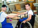 disabled worker in wheelchair in a carpenter's workshop with his colleague